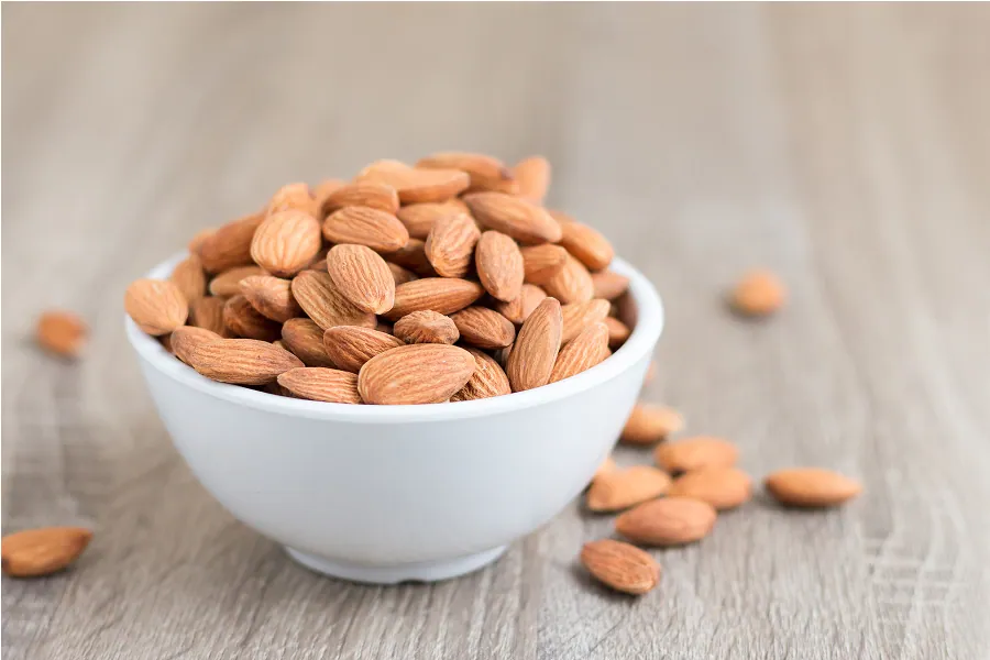 A bowl overflowing with whole, raw almonds, showcasing their natural texture.